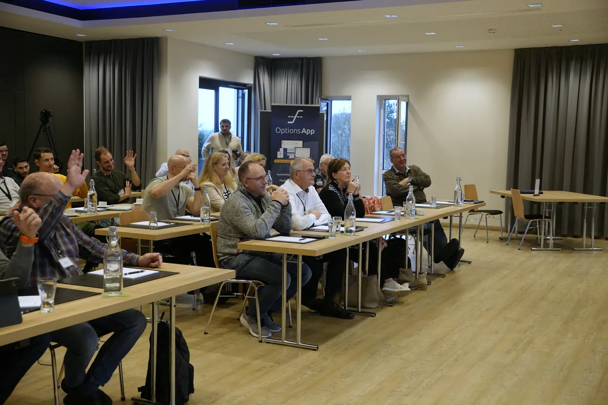 Teilnehmer eines Kundenevents der Legrand Investment GmbH an ihren Tischen, einige melden sich